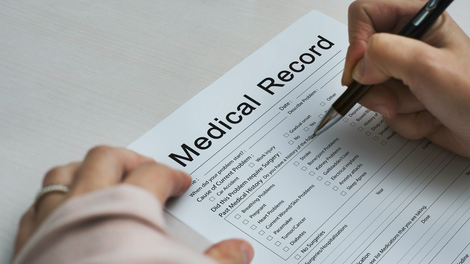 A person filling out a medical record intake form with a pen